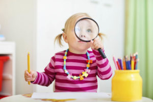 Funny photo of adorable toddler girl looking through magnifier